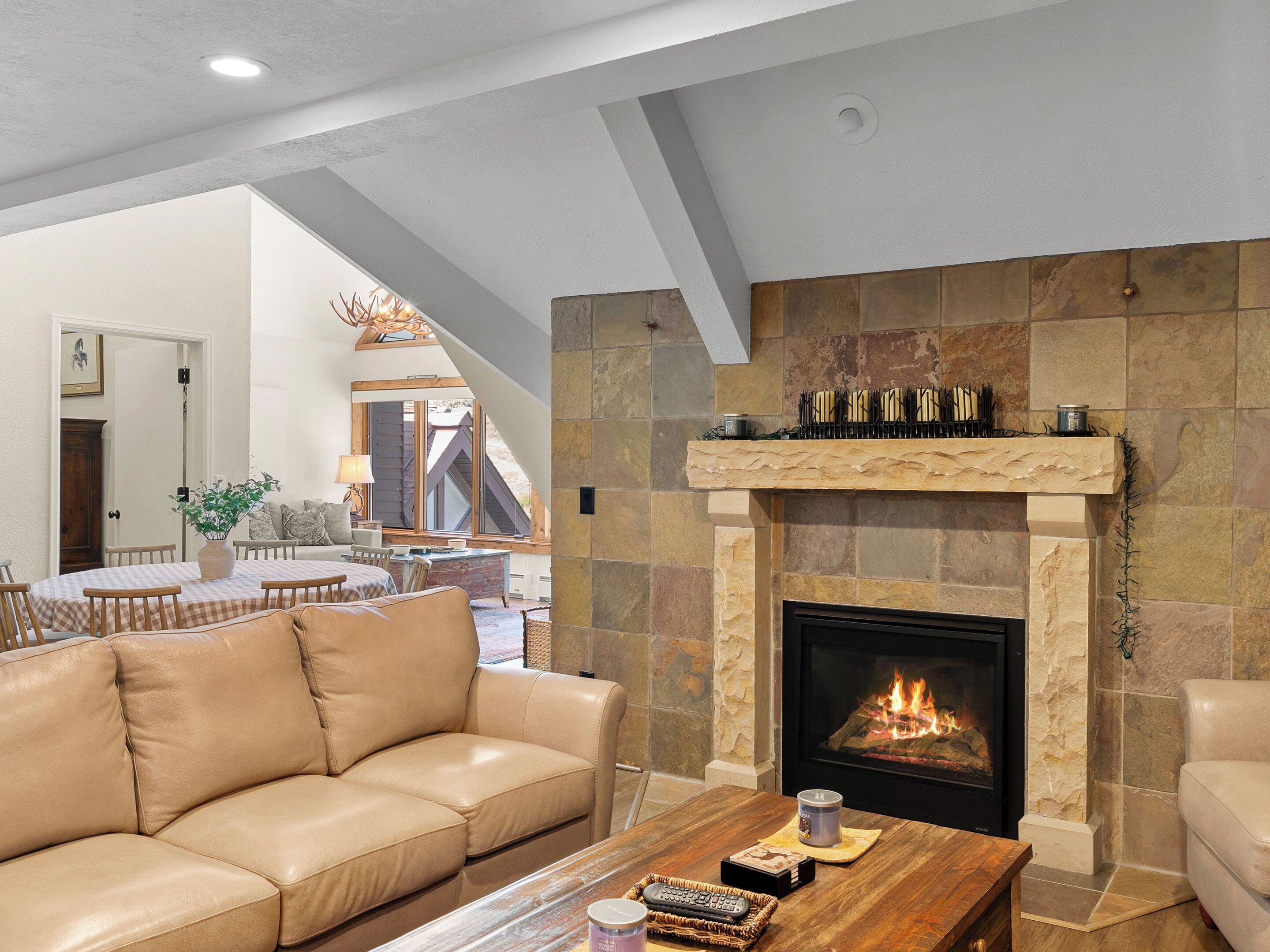 Una sala de estar moderna con chimenea, un sofá de cuero, una mesa de centro de madera y un comedor con mantel a cuadros.