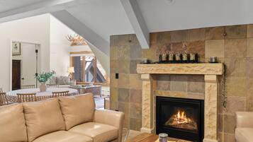 Un salon moderne avec une cheminée, un canapé en cuir, une table basse en bois et un coin repas avec une nappe à carreaux.