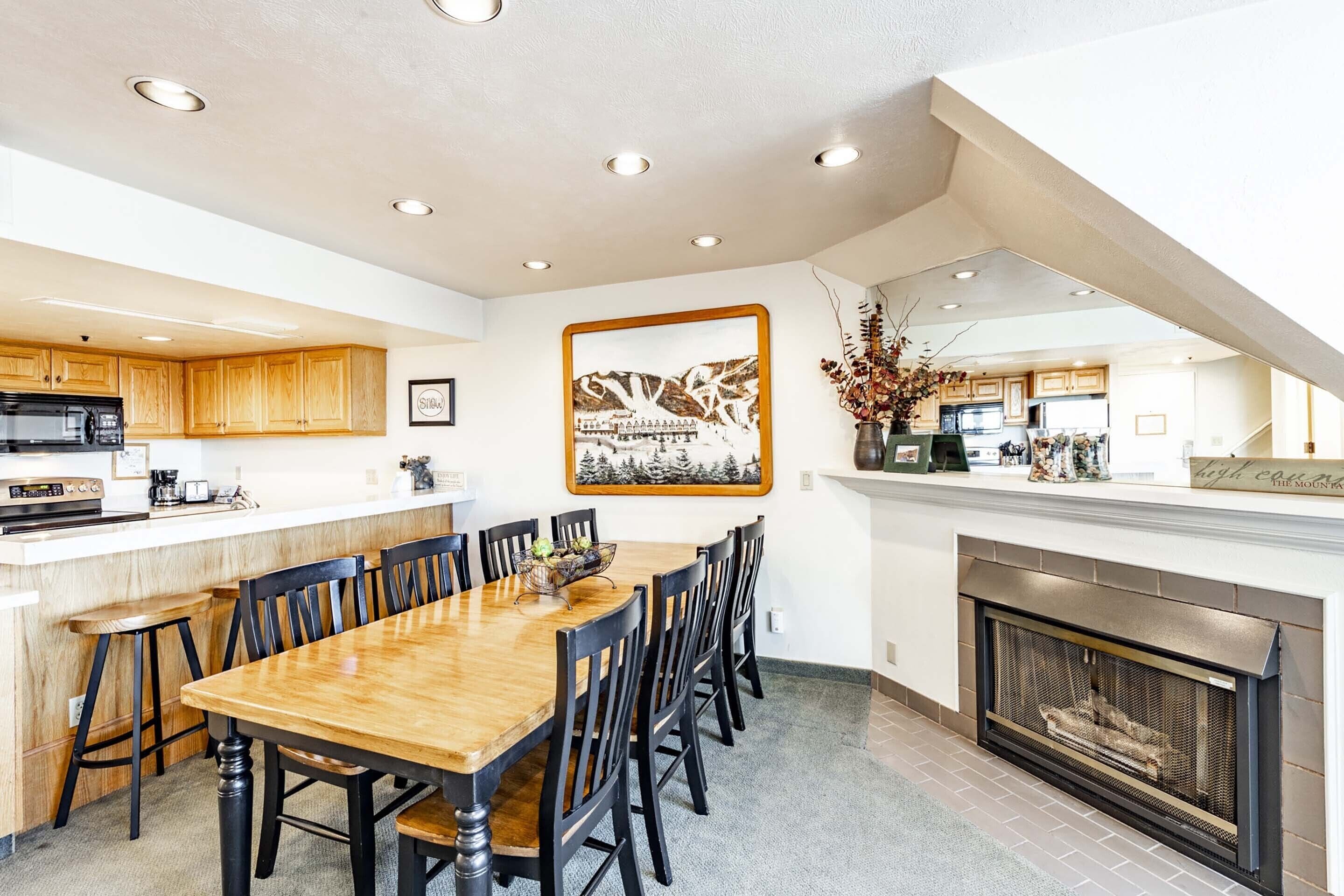 A modern kitchen with wooden cabinets, a dining table with chairs, a fireplace, and recessed ceiling lights.