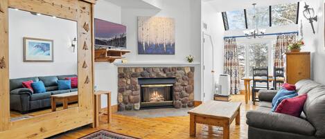 Amplia sala de estar con chimenea de piedra, piso de madera y un ventanal con vistas al exterior.