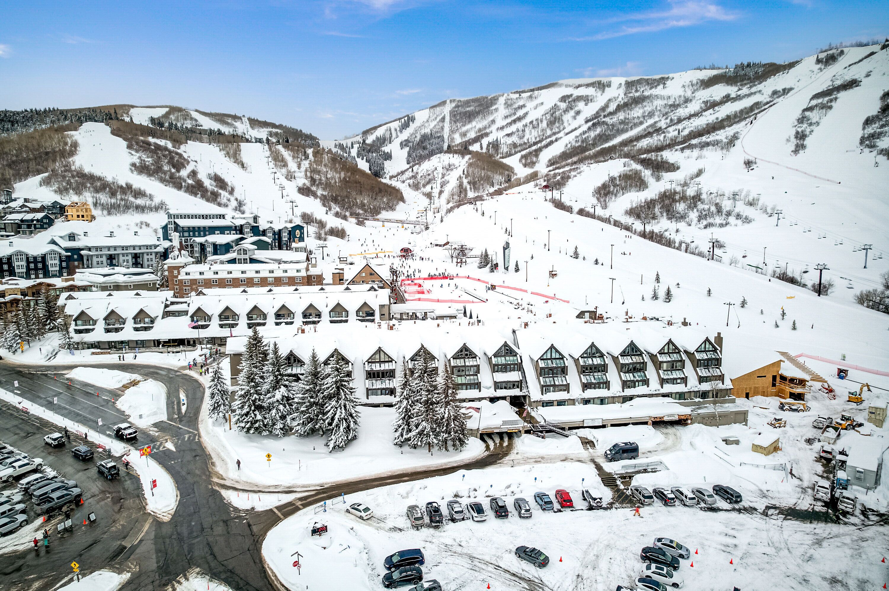 Une station de ski dotée d’un grand bâtiment avec de nombreuses fenêtres, d’un parking et d’une piste de ski.