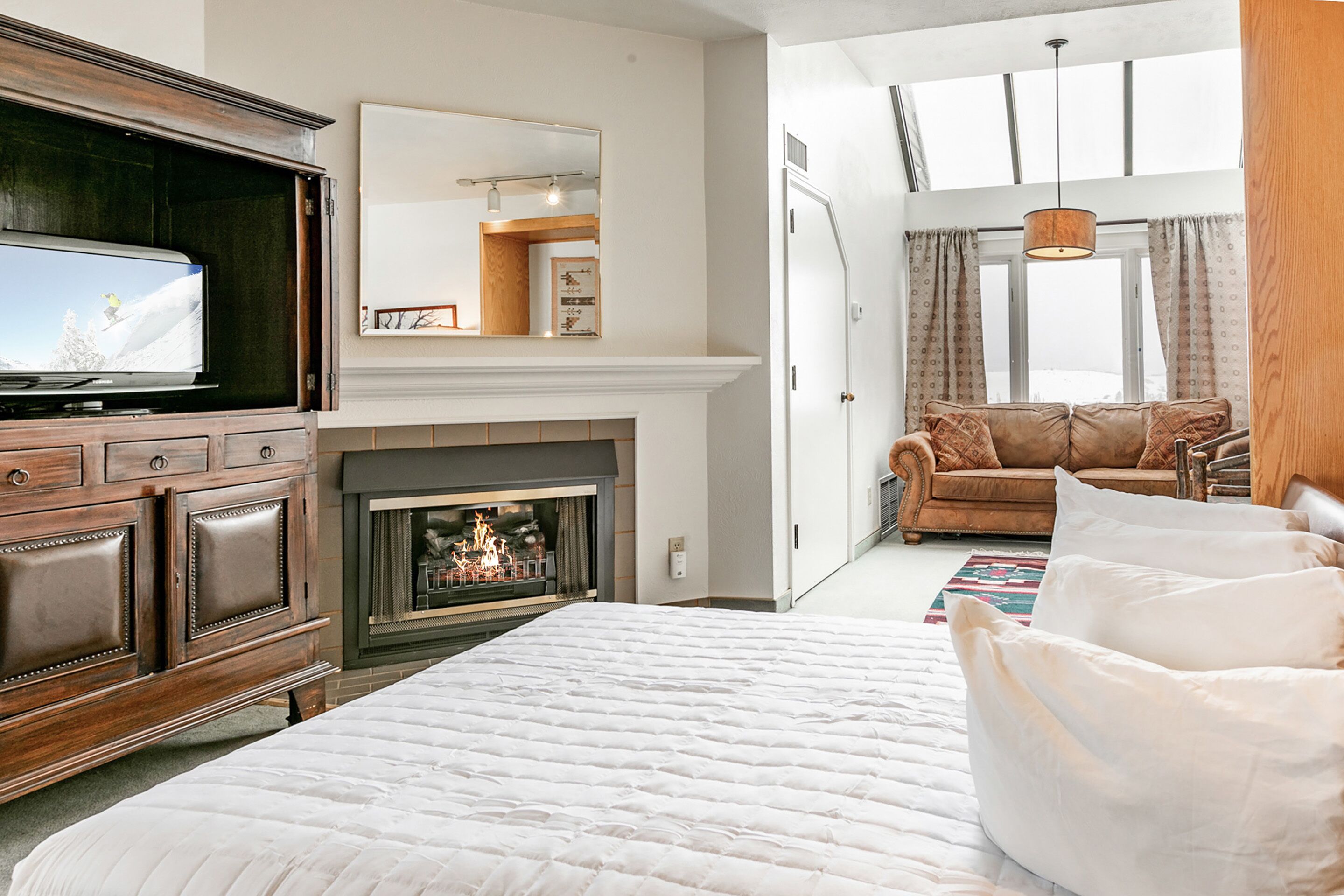 A bedroom with a large bed, a TV, a fireplace, a sofa, and a window with curtains.