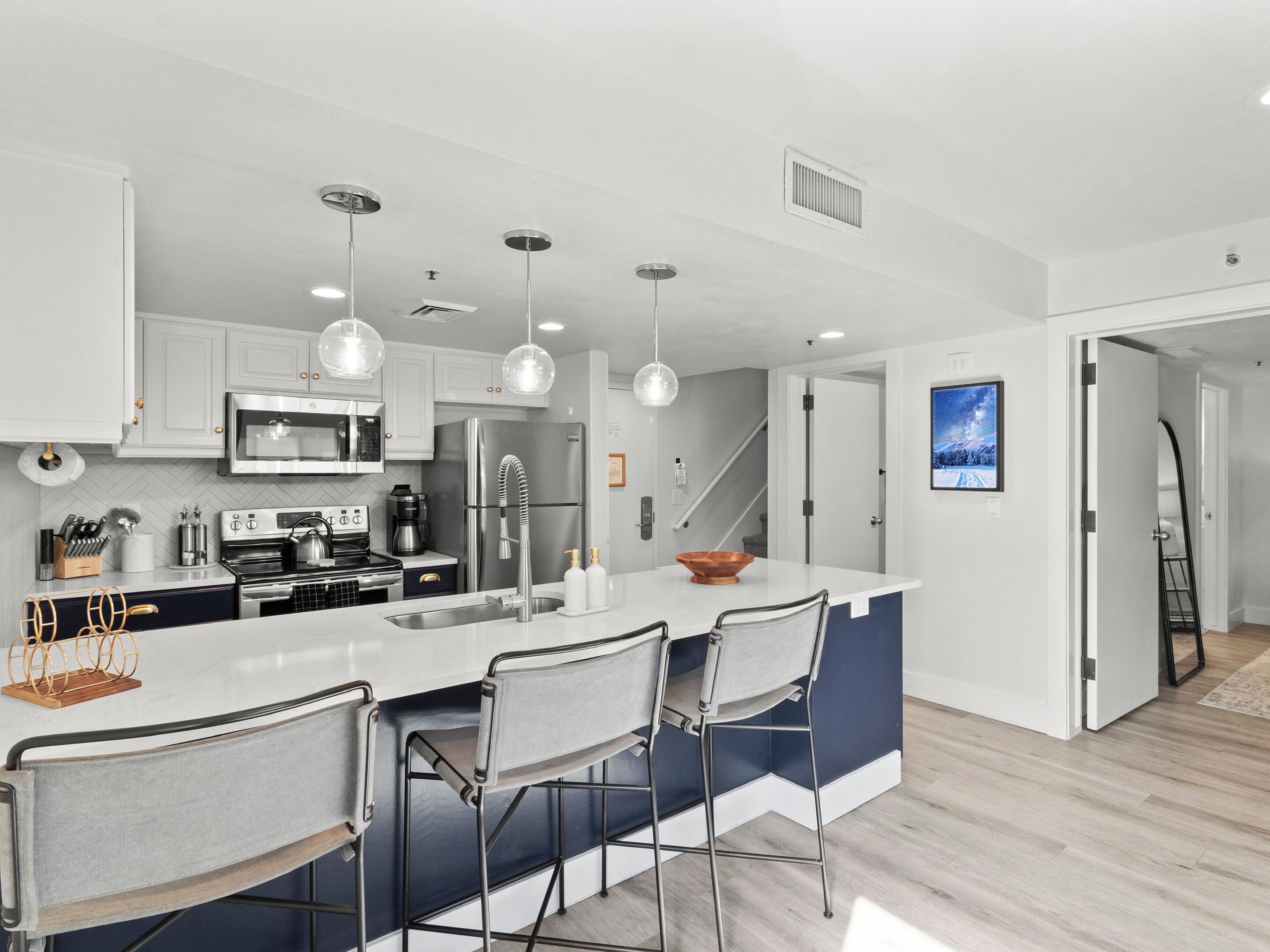 Una cocina moderna con armarios blancos, electrodomésticos de acero inoxidable y una isla central con taburetes de bar.
