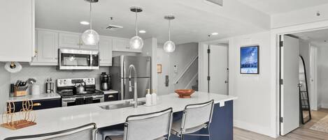 Una cocina moderna con armarios blancos, electrodomésticos de acero inoxidable y una isla central con taburetes de bar.