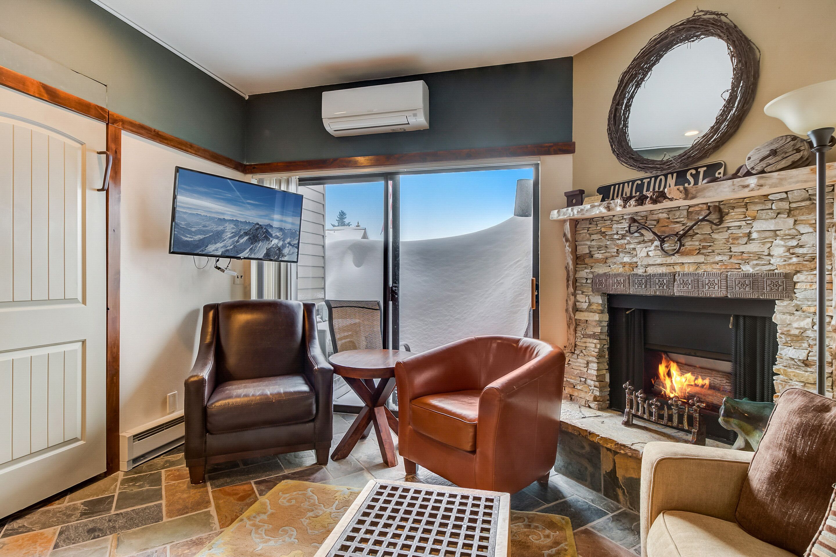 A living room with leather chairs, a stone fireplace, a flat-screen TV, and a view of the mountains.