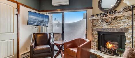 A living room with leather chairs, a stone fireplace, a flat-screen TV, and a view of the mountains.