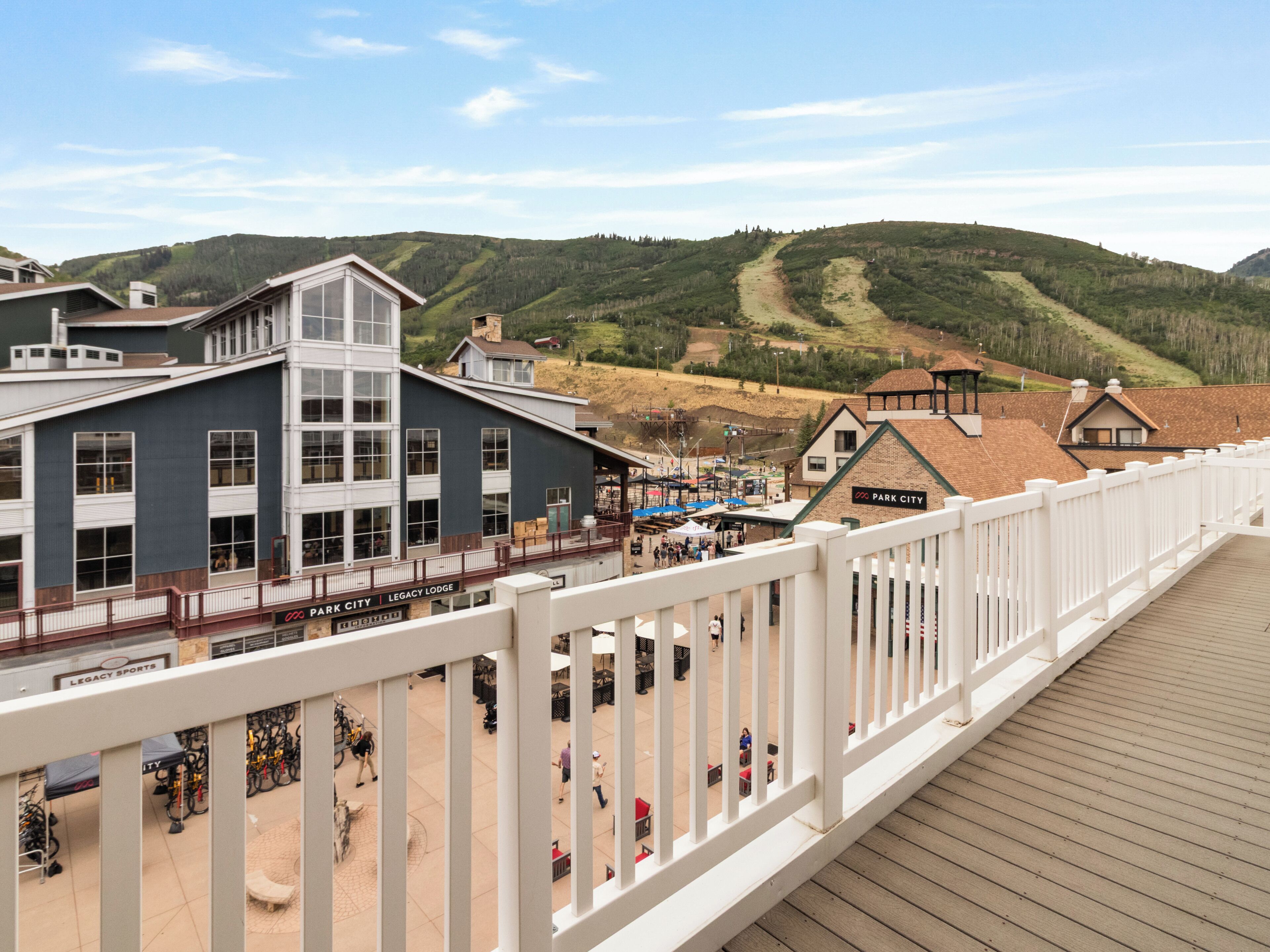 A view of a hotel with a deck overlooking a mountainous landscape, featuring a restaurant and a sign for 'Park City Legacy Lodge.'