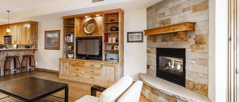 A living room with a stone fireplace, wooden entertainment center, and a ceiling fan.