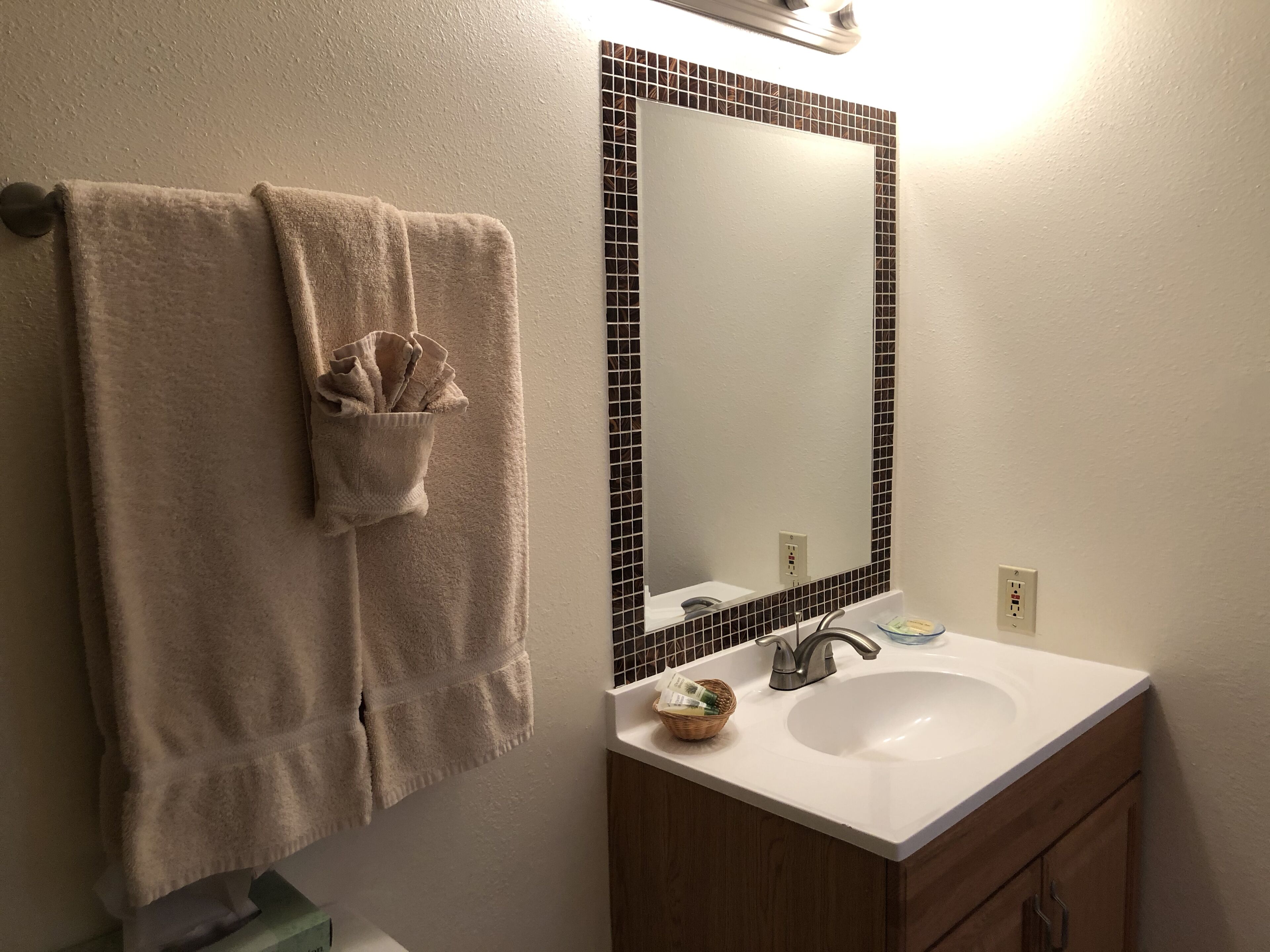A bathroom with a white sink, a mirror with black tile framing, and a towel rack with a folded towel.
