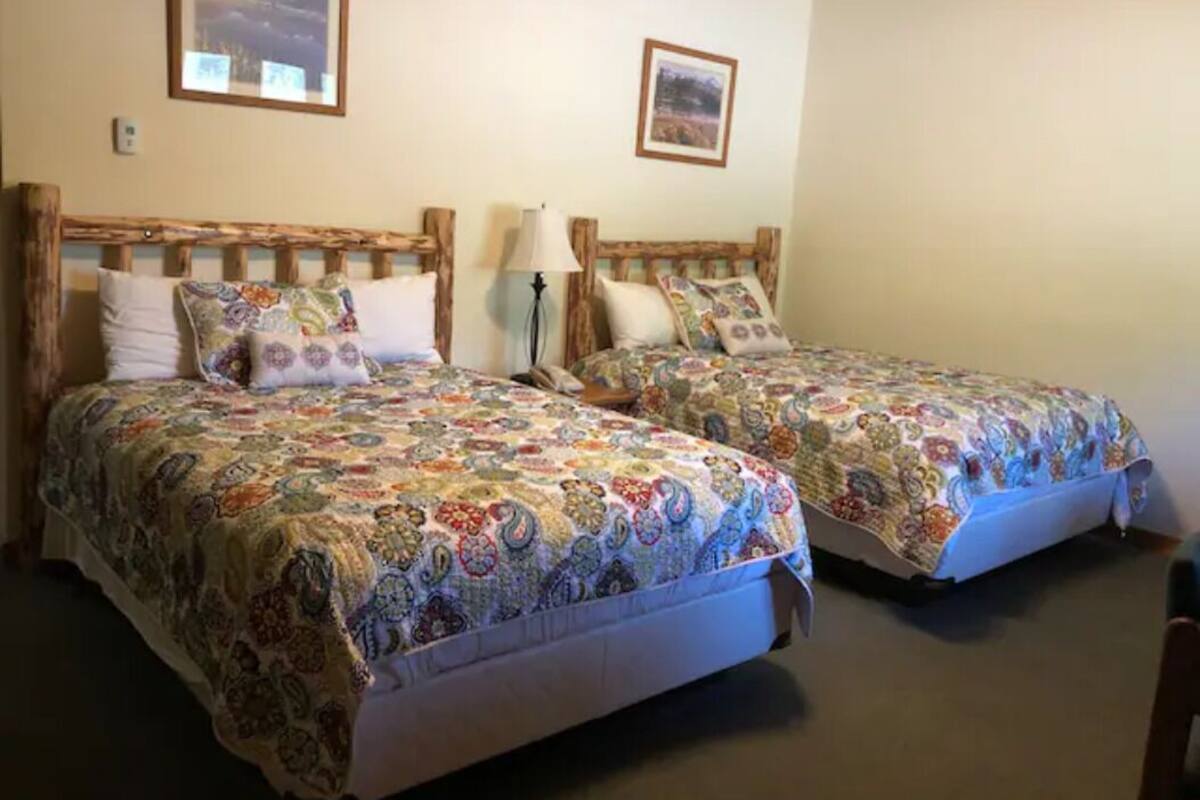 Two single beds with wooden headboards, each with a colorful quilt and a bedside lamp.