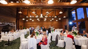 A banquet hall with round tables, white chairs, and chandeliers. - Dao House (Estes Park)
