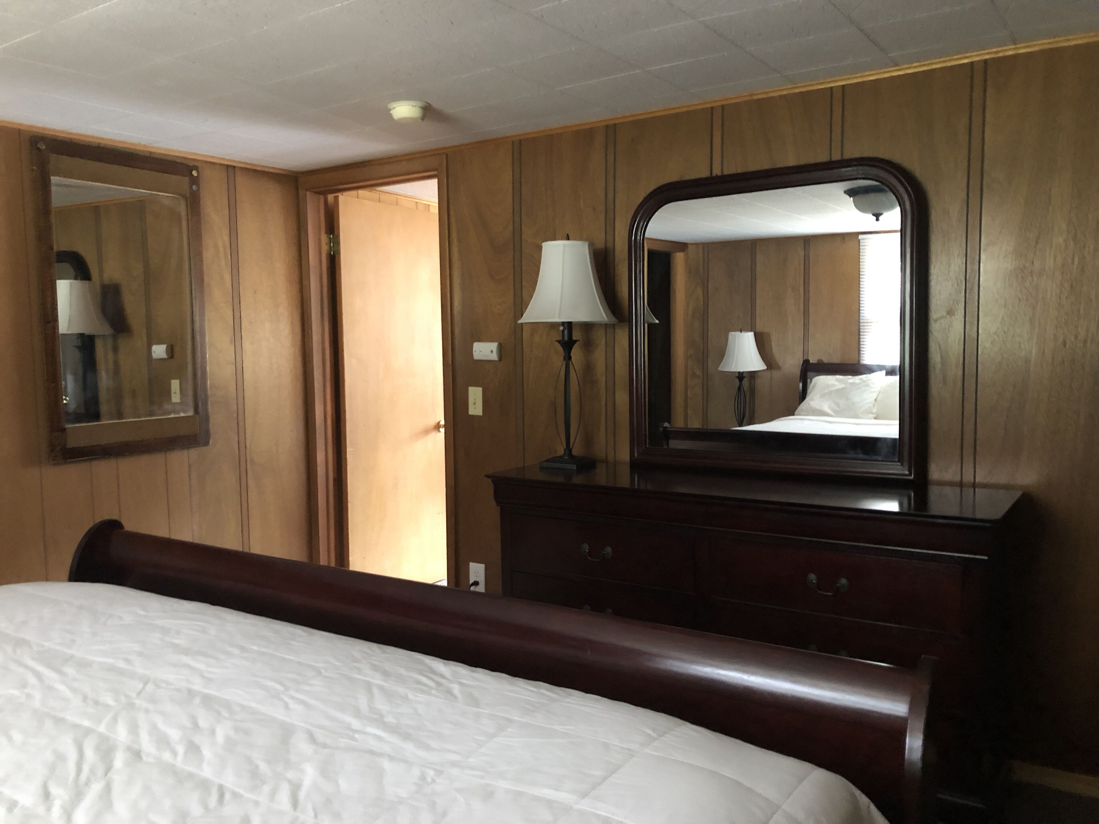 Een hotelkamer met een houten lambrisering, een groot bed met een witte dekbedovertrek, een dressoir met spiegel en twee bedlampjes.