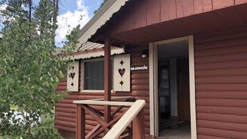 A wooden cabin with a porch, a window with heart-shaped cutouts, and a door with a sign.
