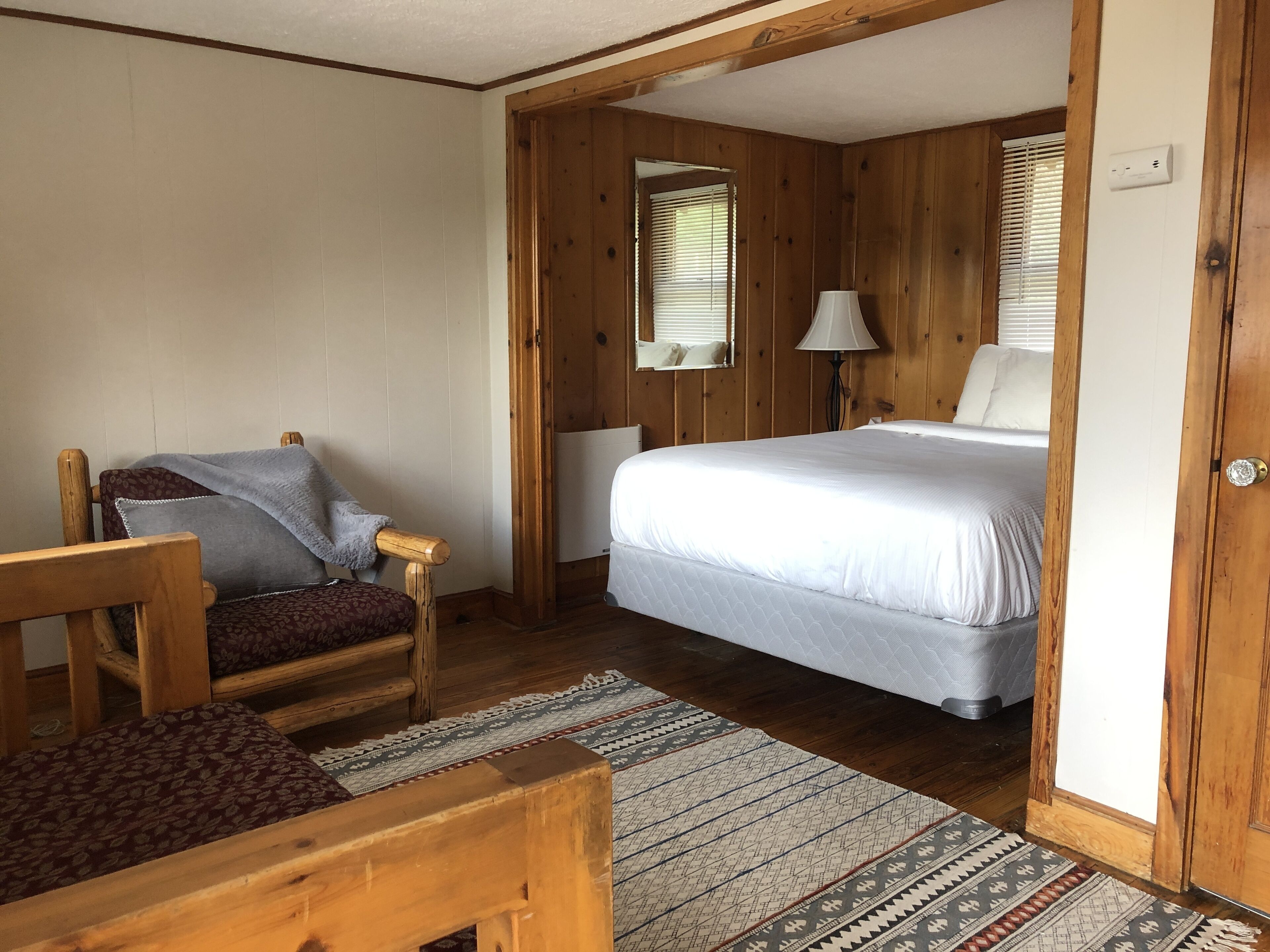 A wooden room with a bed, a chair, a lamp, and a window.