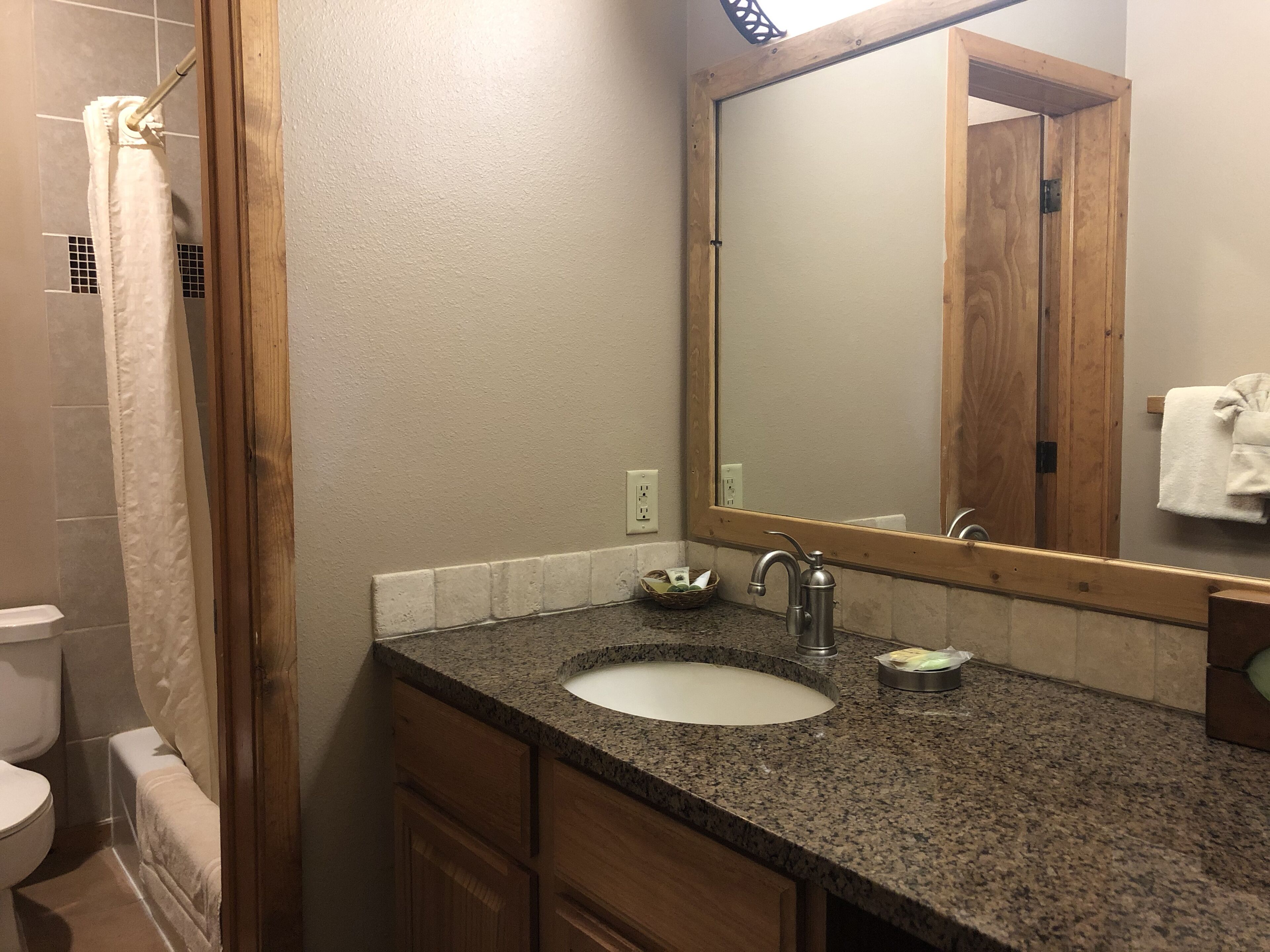 Une salle de bain avec un comptoir en granit, un lavabo, un miroir et des armoires en bois.