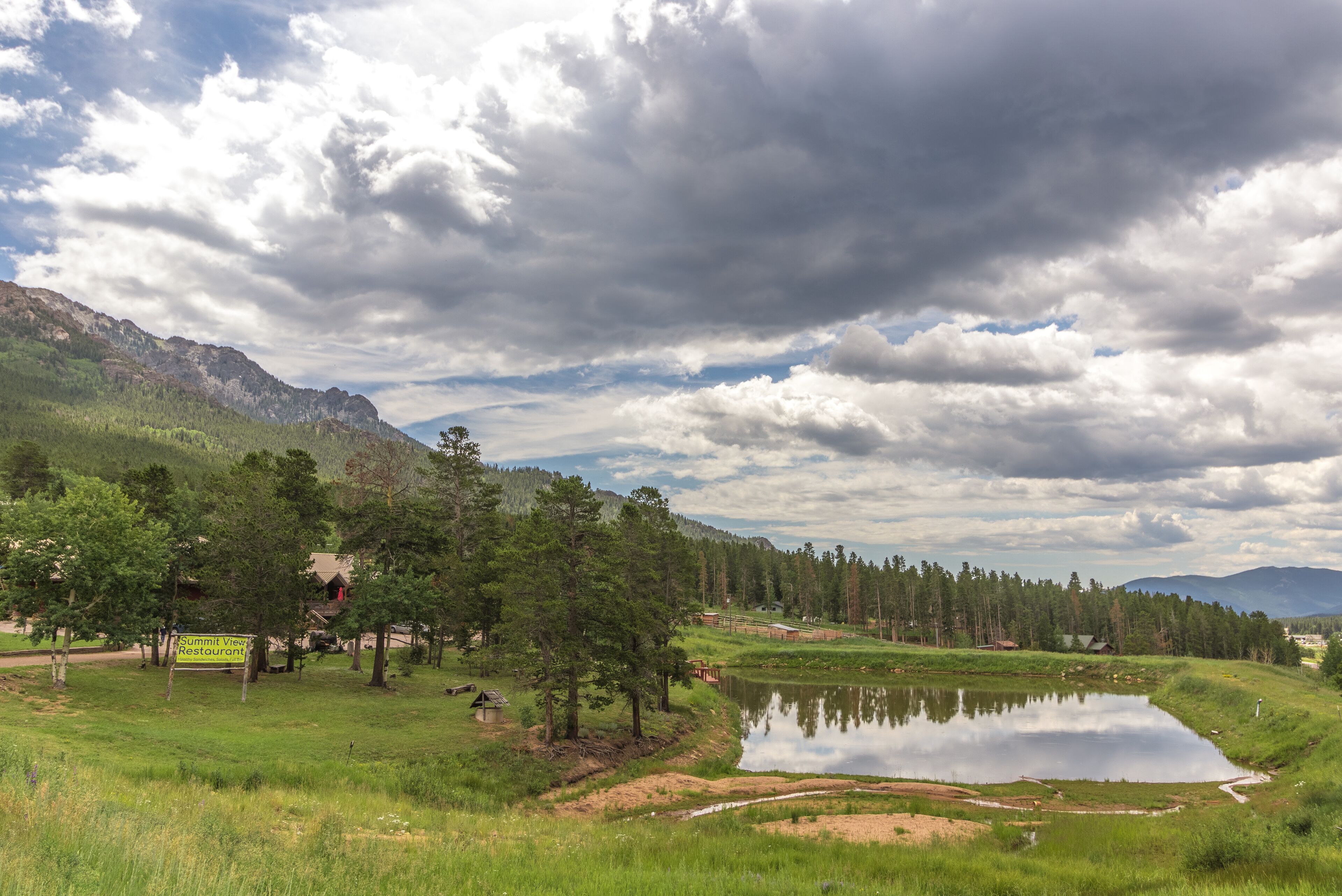 A mountain landscape with a pond, trees, and a restaurant sign.