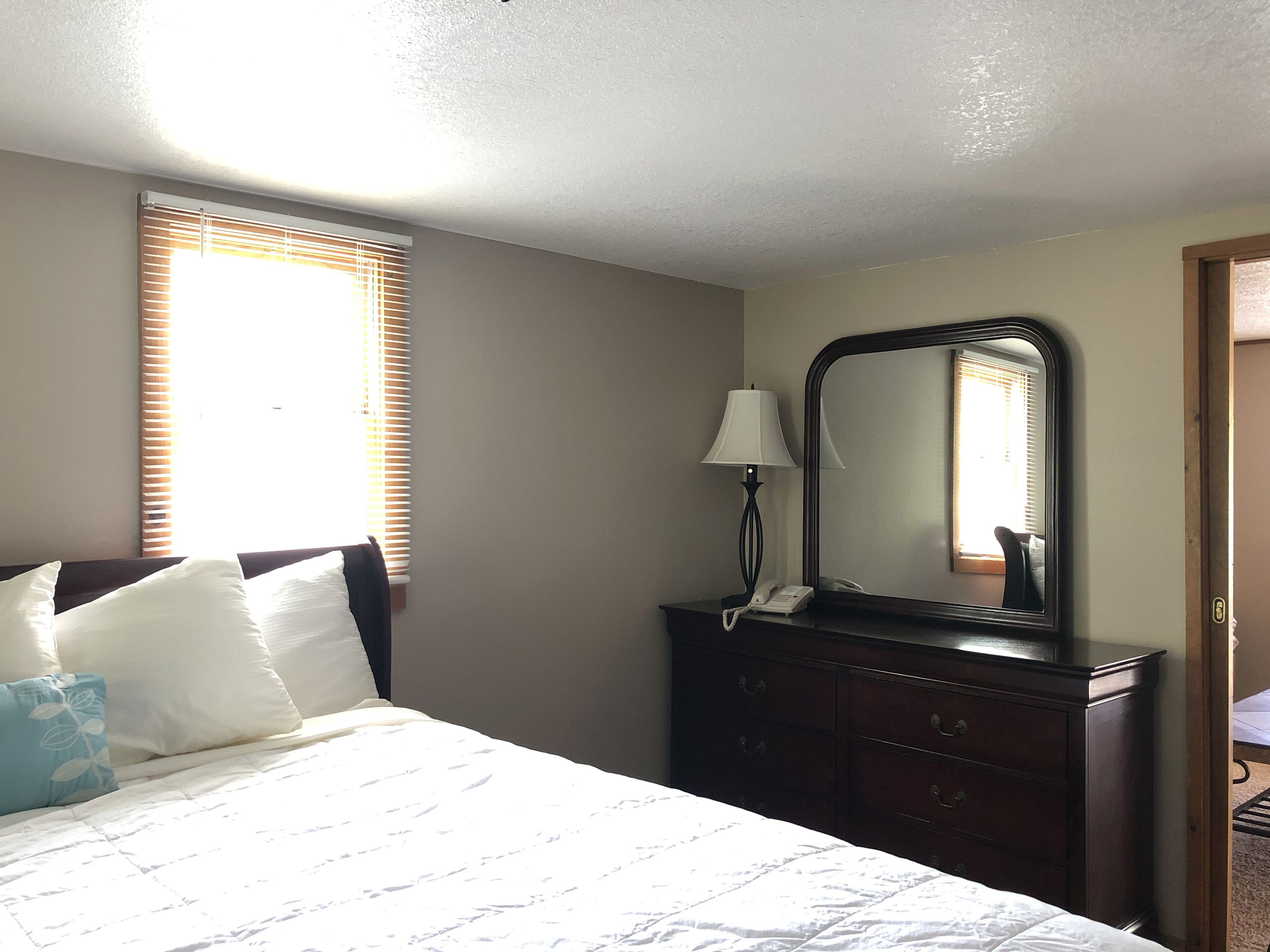 A bedroom with a bed, a dresser, a mirror, and a window with blinds.