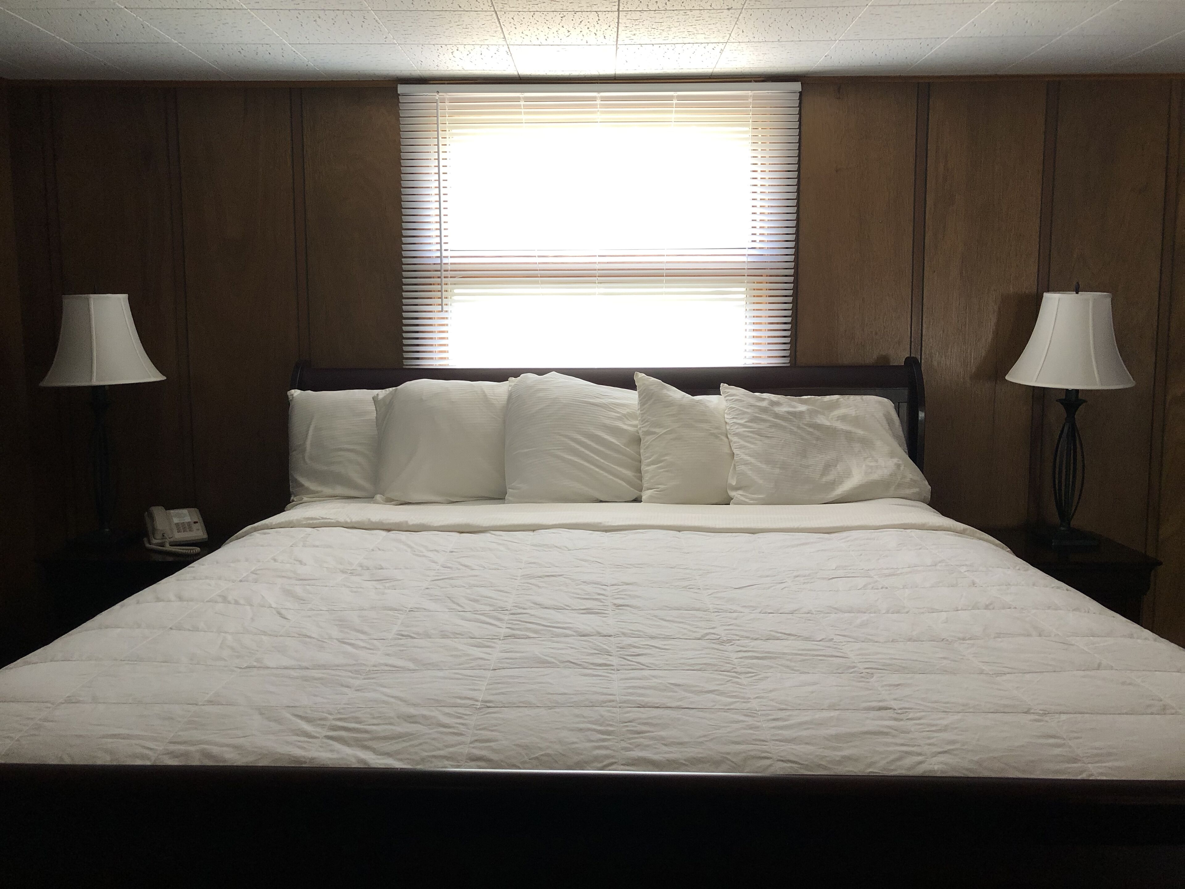 A neatly made bed with white linens, a wooden headboard, and two bedside lamps.