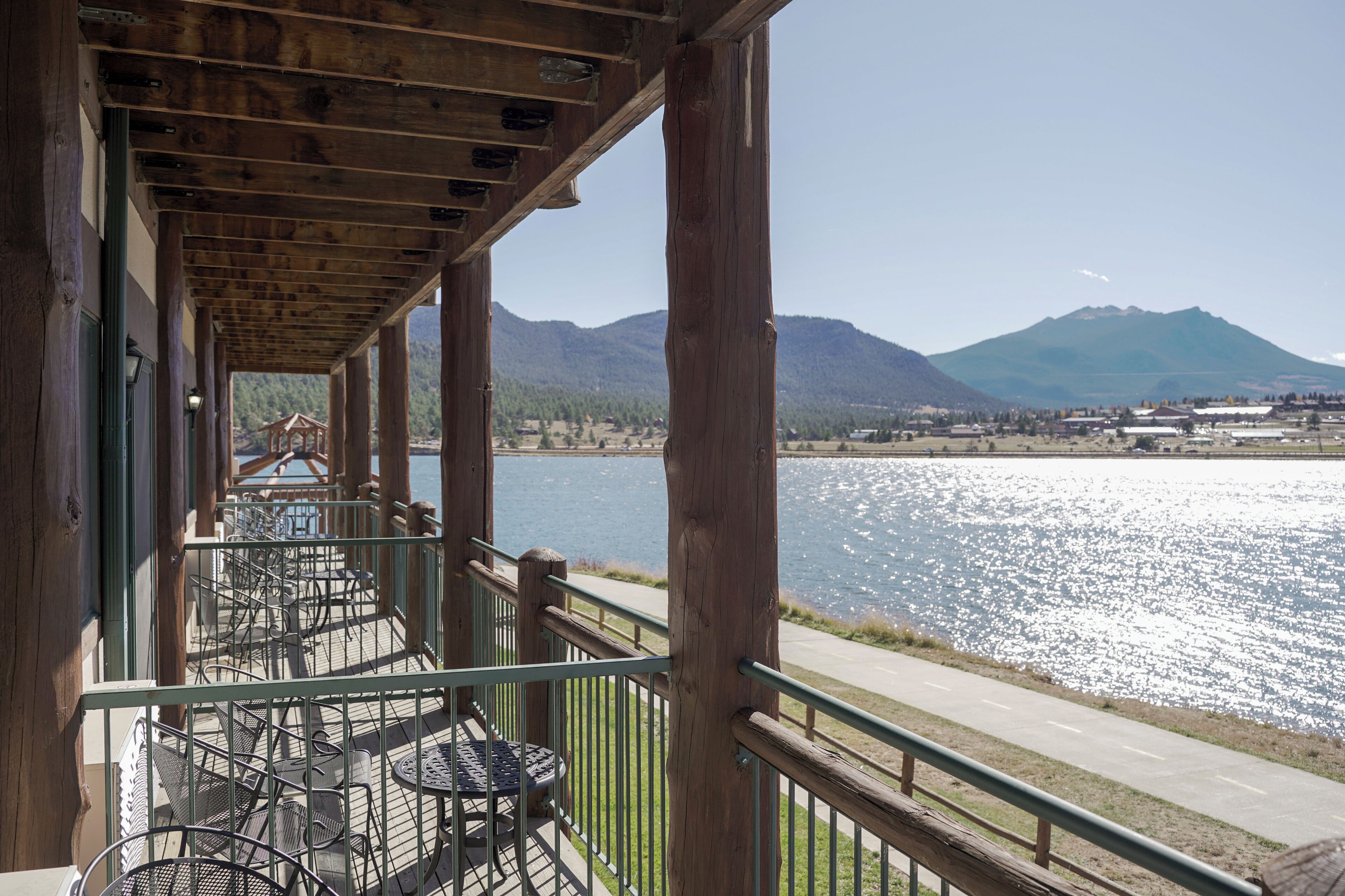 A wooden deck with metal railings overlooking a lake with mountains in the background.