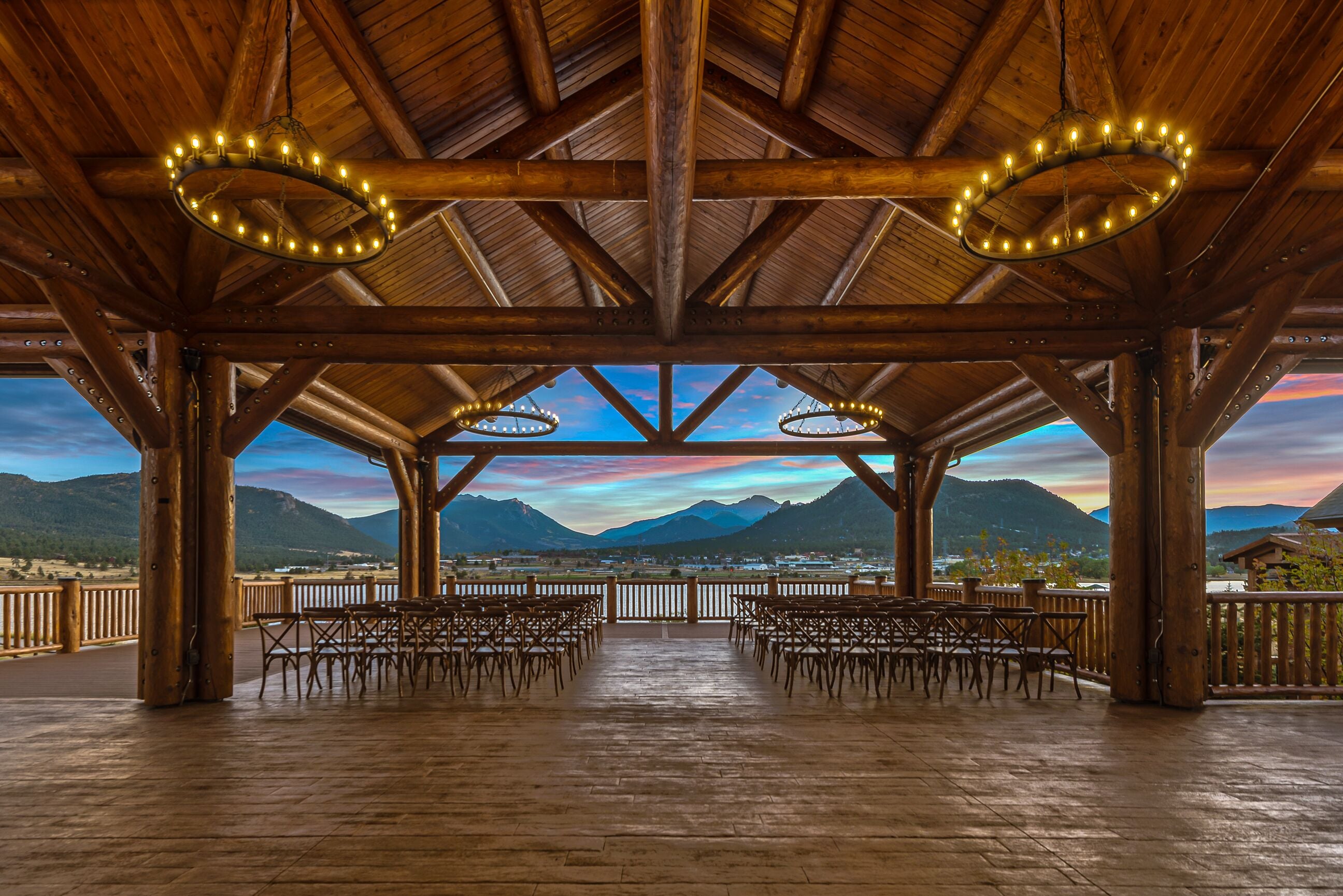 A wooden pavilion with a view of mountains and a sunset.