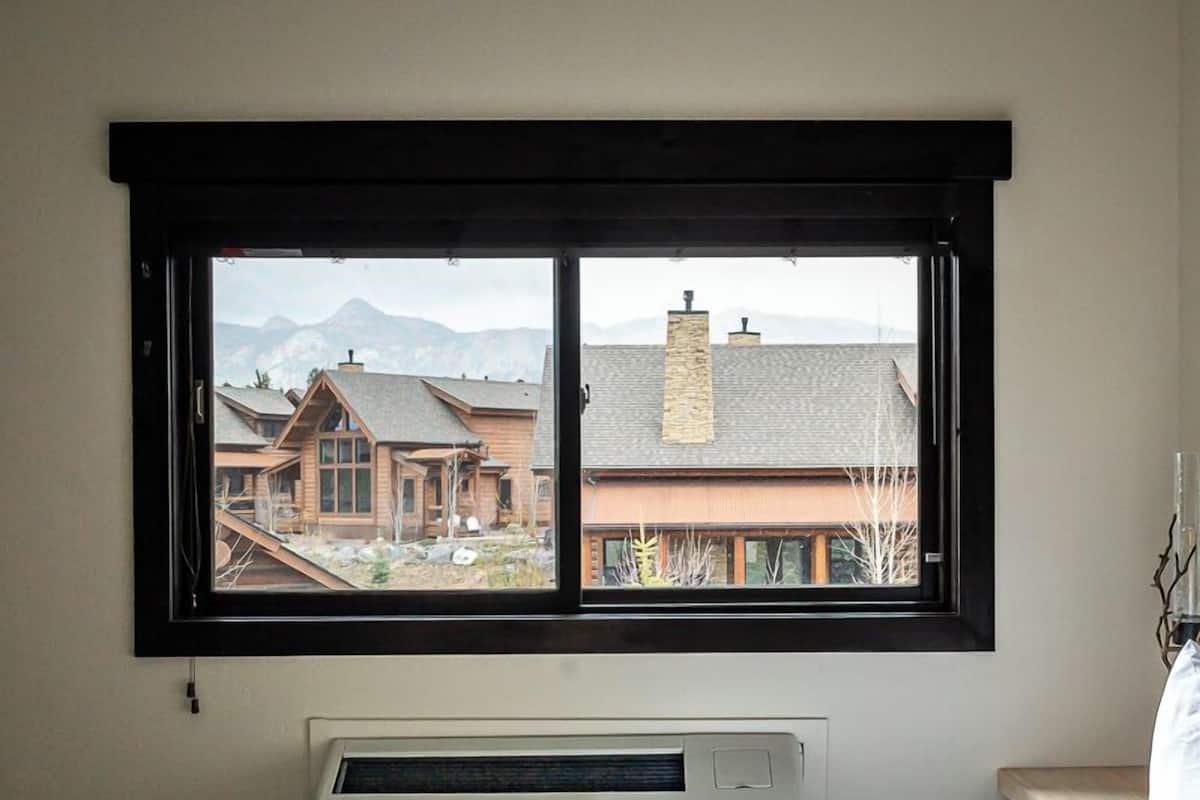 A bedroom with a large window, a bed with a fur throw, and a thermostat on the wall.