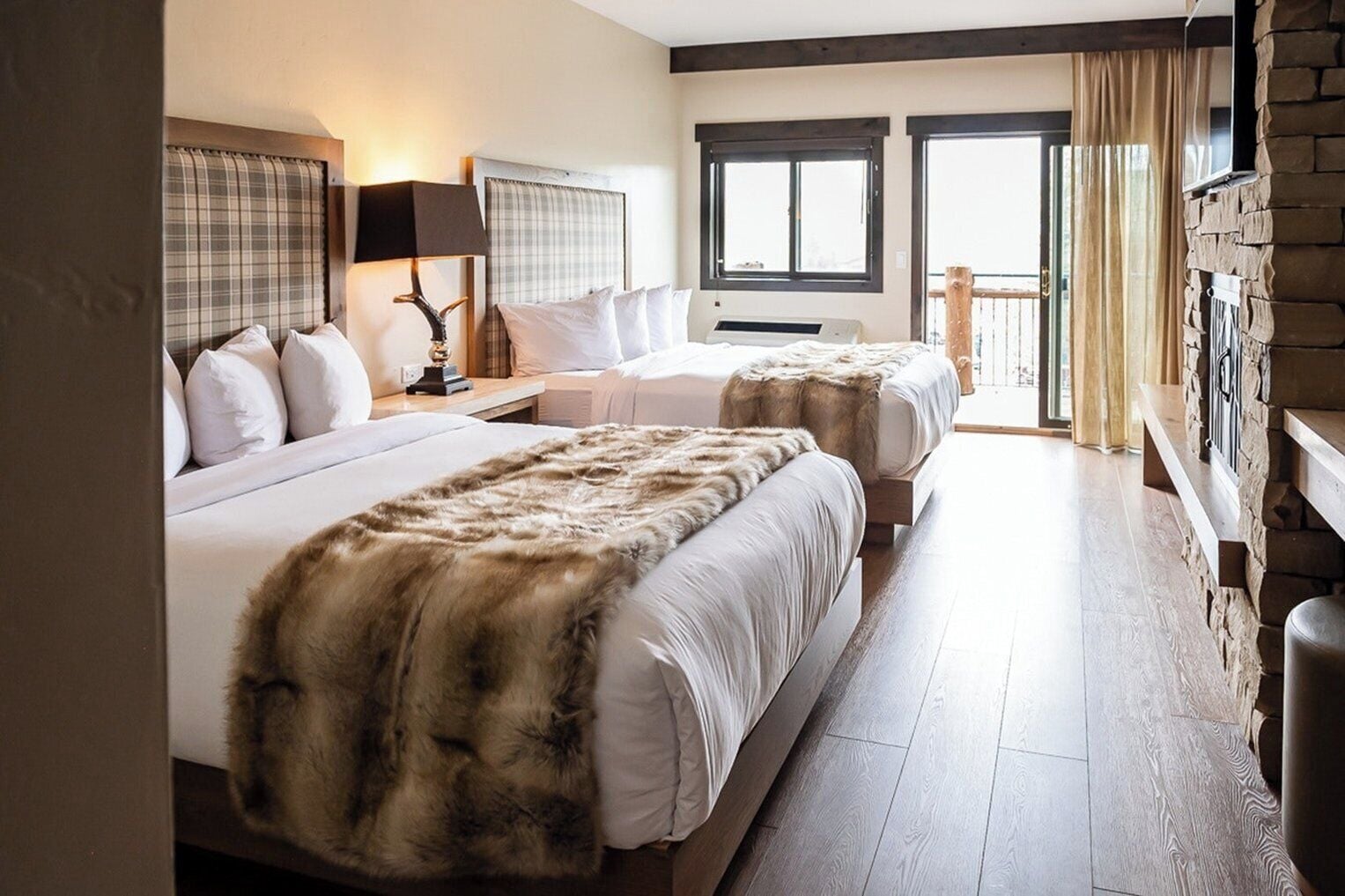 Habitación de hotel con dos camas, chimenea de piedra y balcón con cortinas.