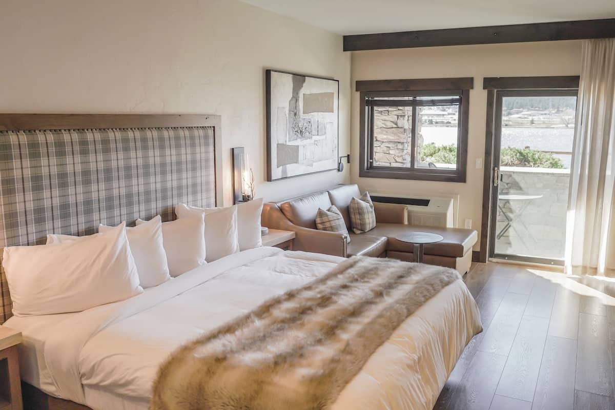 A hotel room with a bed, a sofa, a small table, and a view of the outdoors.