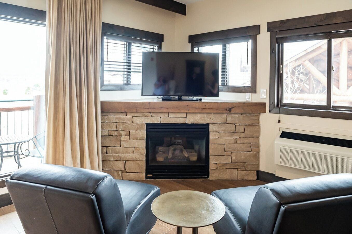 A living room with a stone fireplace, a flat-screen TV on a wooden mantel, leather sofas, and a small round table.