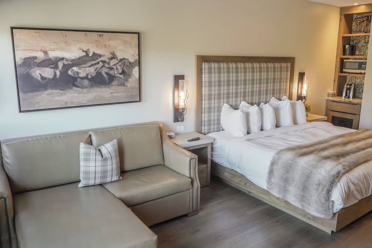 A bedroom with a bed, a sofa, a painting, bedside lamps, and a nightstand.