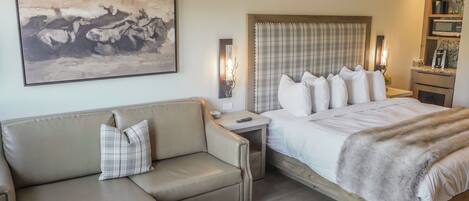 A bedroom with a bed, a sofa, a painting, bedside lamps, and a nightstand.