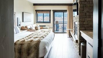 A hotel room with a large bed, a balcony with a view, and a stone wall.