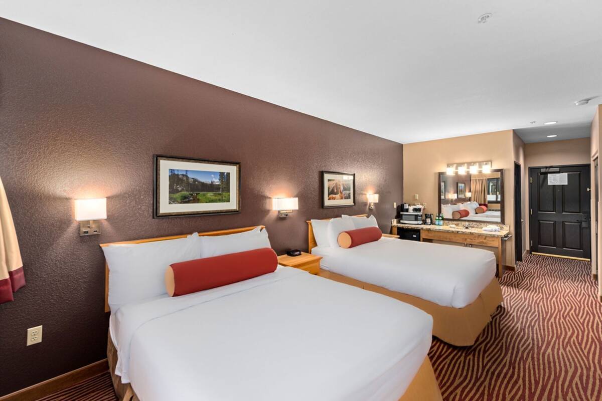 A hotel room with two beds, a desk with a mirror, and a kitchenette.