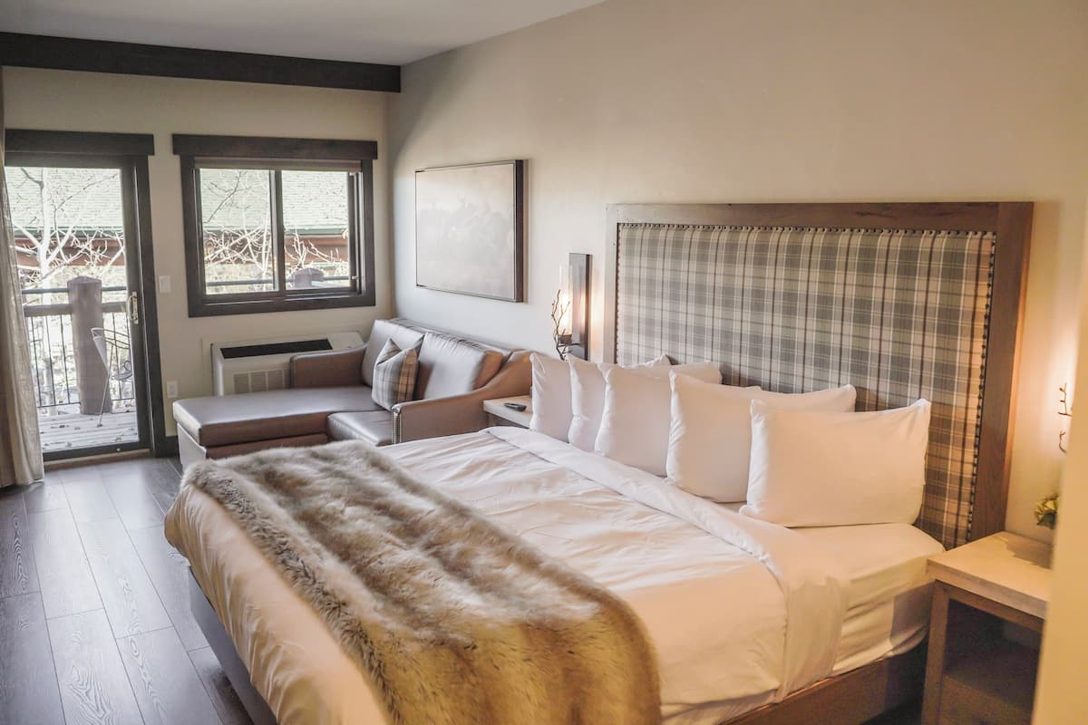 A bedroom with a bed, a sofa, a headboard, a window, and a door.