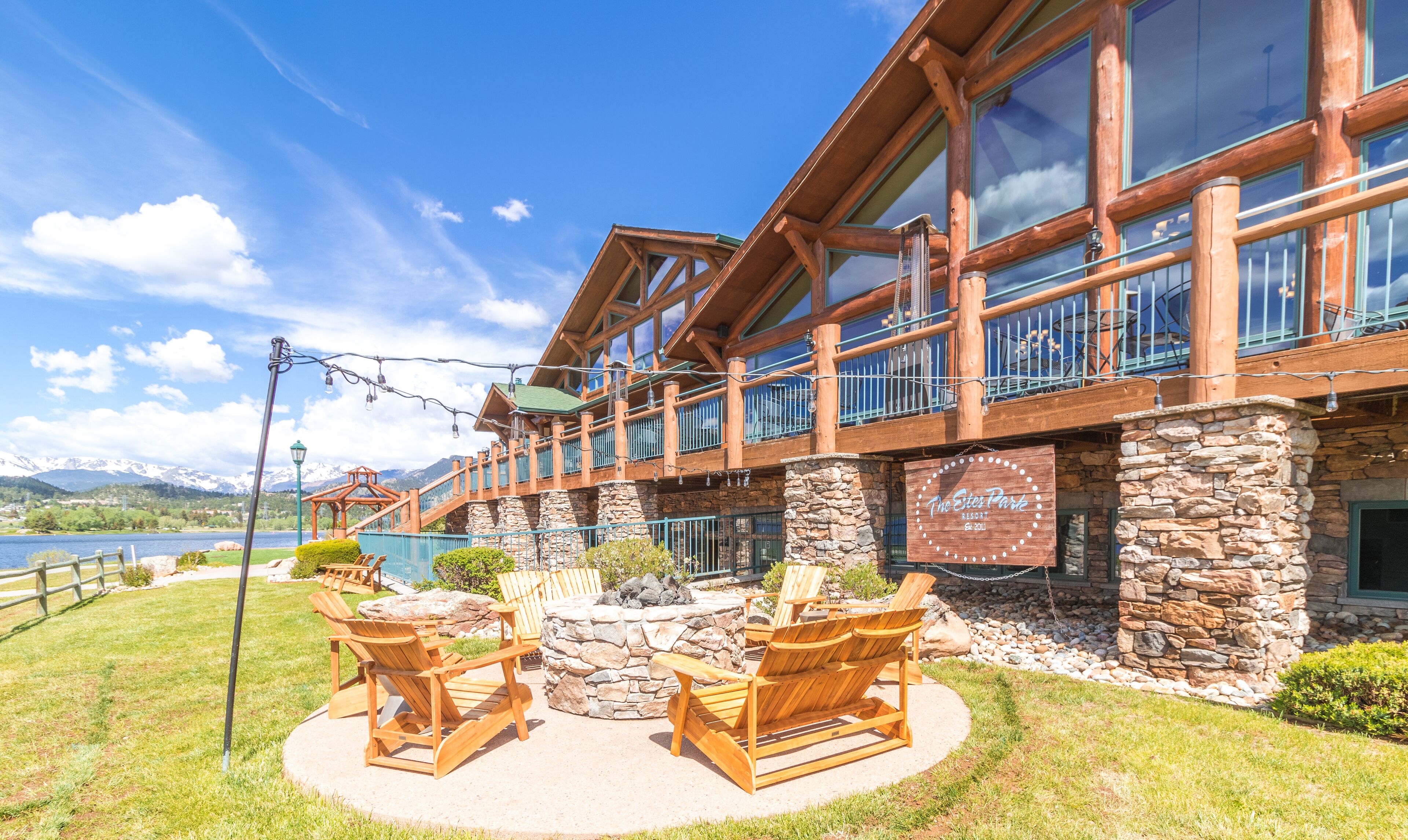 A lodge with a stone facade, wooden balconies, and outdoor seating by a lake.