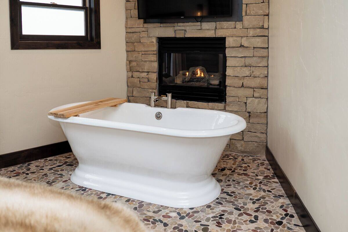 A white freestanding bathtub in a bathroom with a stone wall and a fireplace.