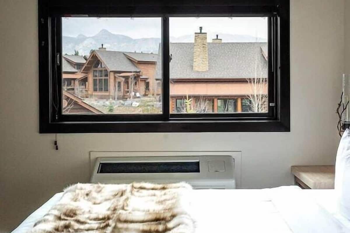 A bedroom with a large window, a bed with a fur throw, and a radiator.