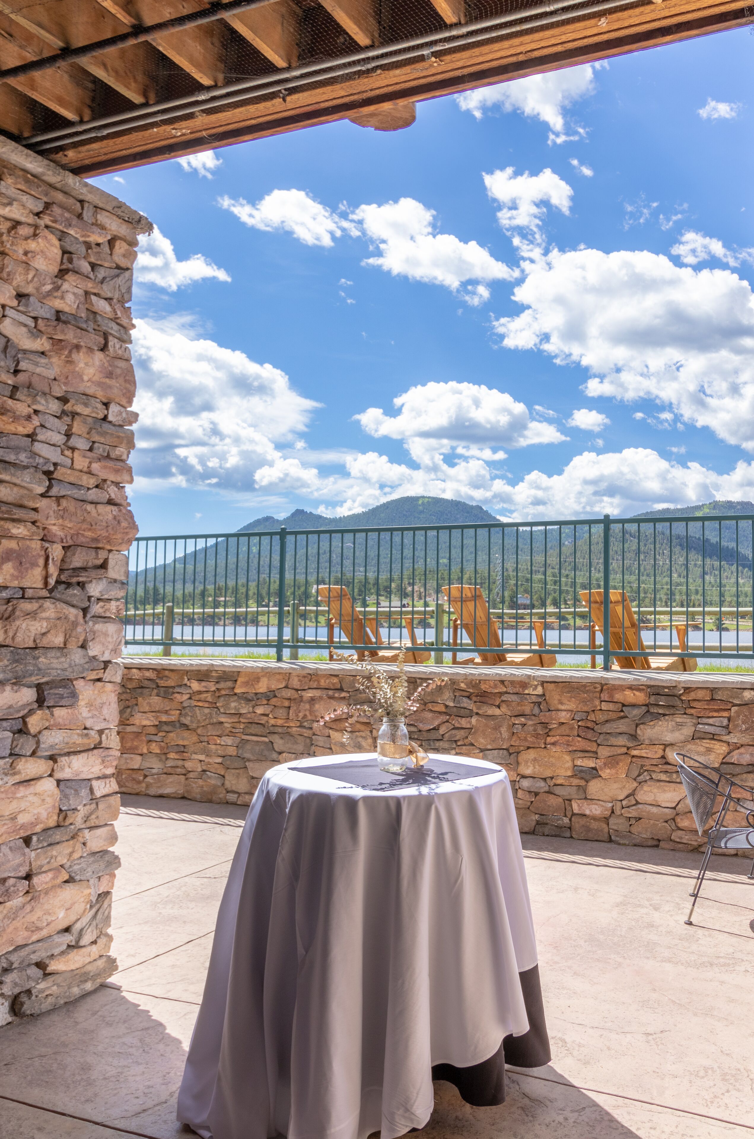 A patio with a table and chairs, a stone wall, and a view of a lake and mountains.