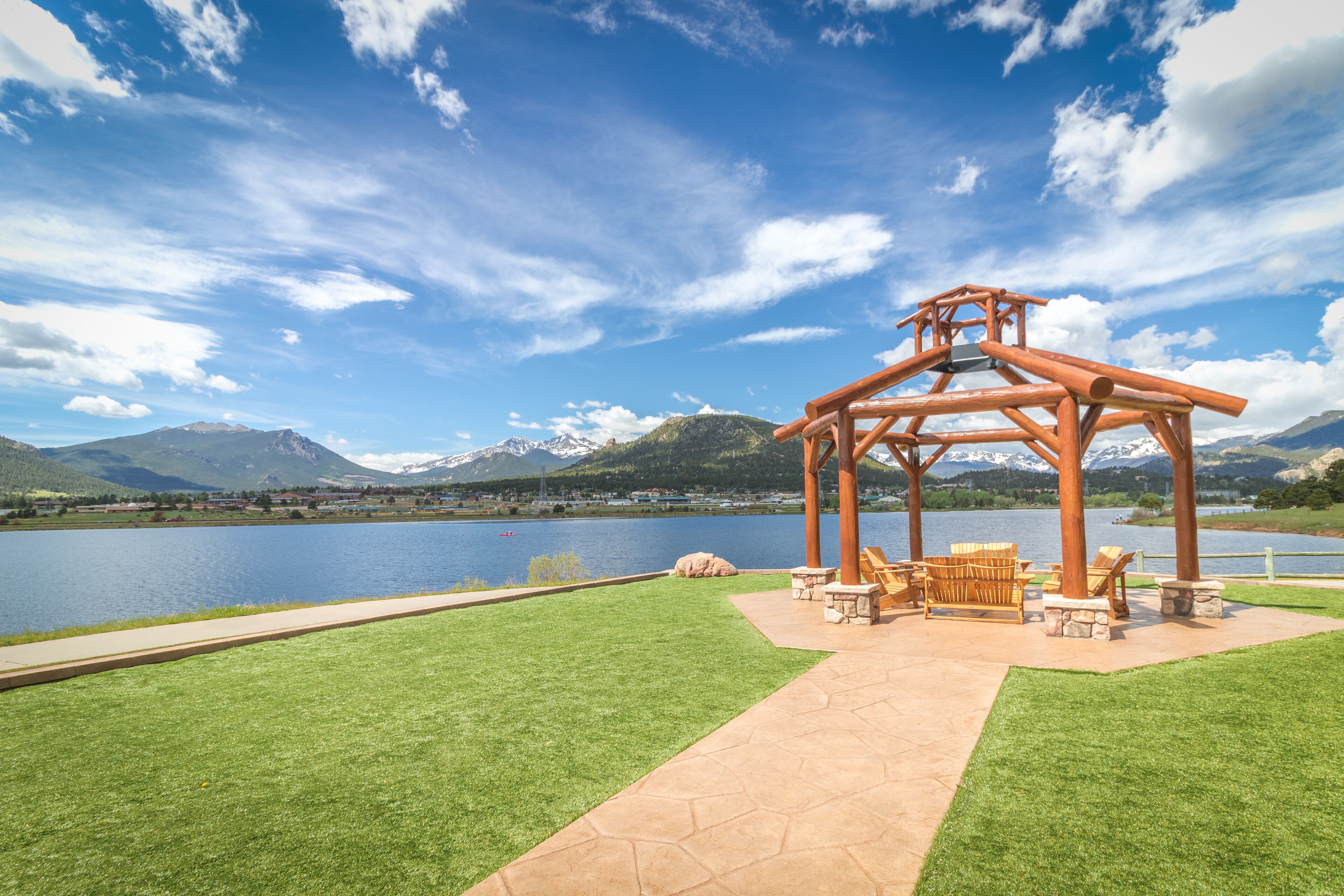 A gazebo with seating, a paved walkway, and a lake with mountains in the background.