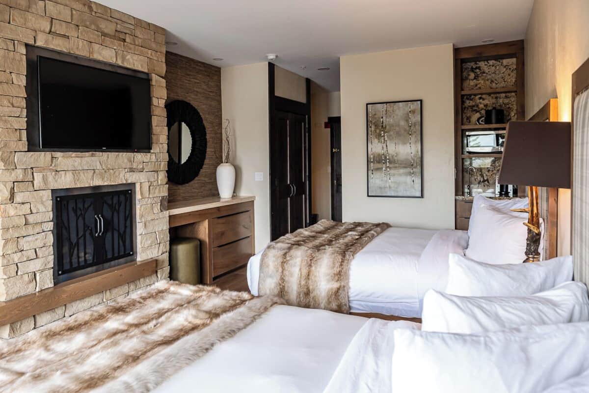A hotel room with two beds, a fireplace, a TV, and a bookshelf.