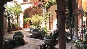 An outdoor courtyard with stone flooring, potted plants, and a central archway.