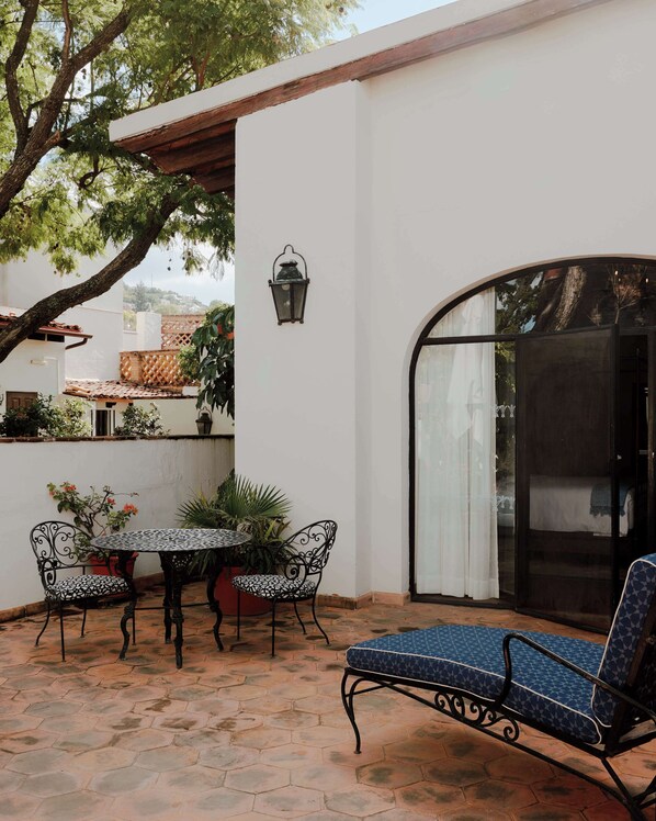 Un patio con una mesa y sillas, un sillón azul acolchado, una planta en maceta y un farol fijado a la pared.