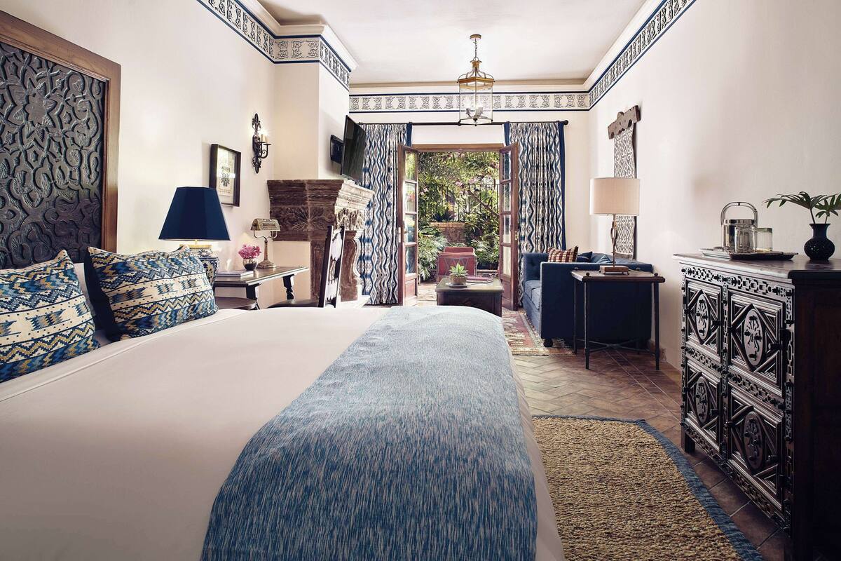 A bedroom with a large bed, a desk, and a view of a garden.