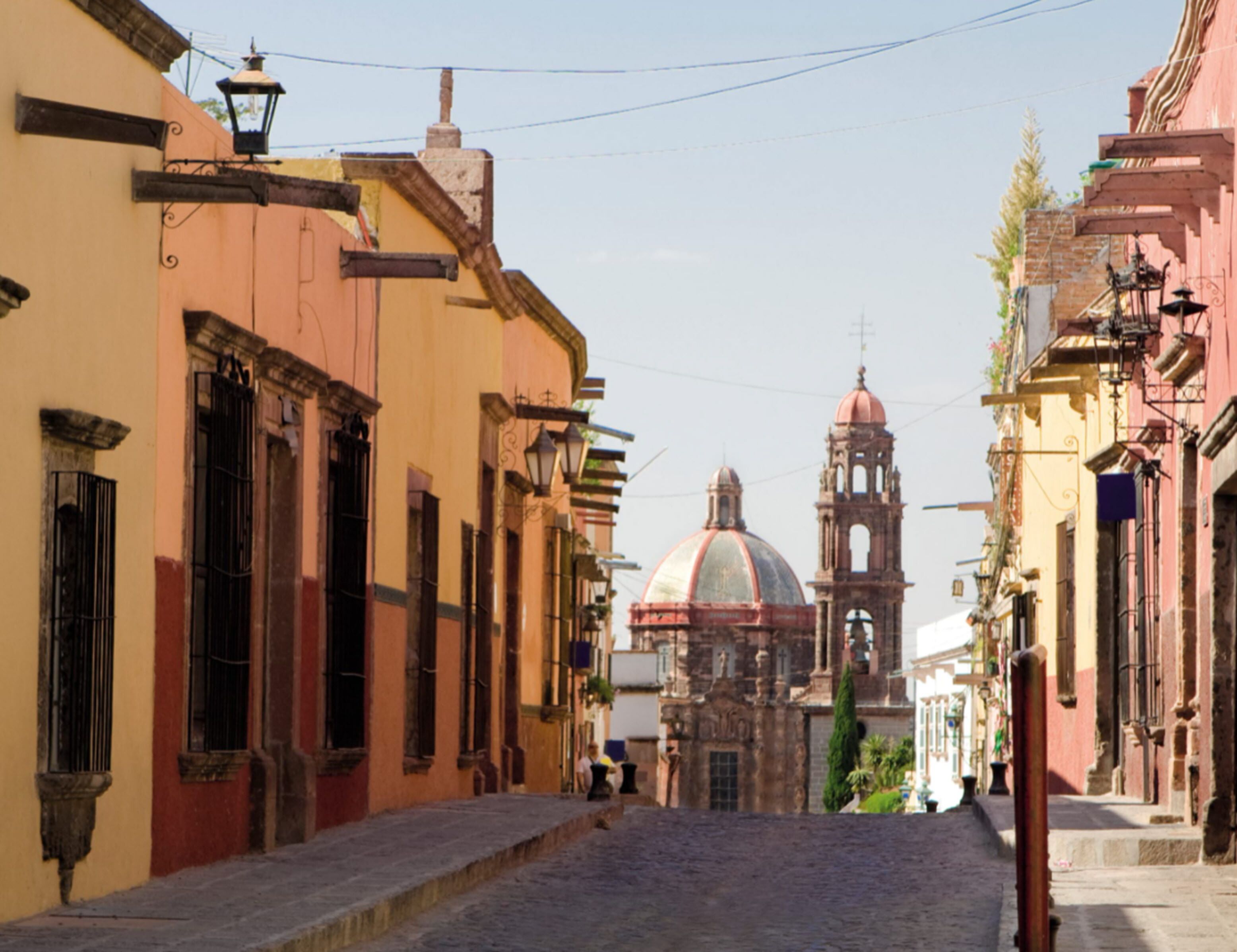 A cobblestone street lined with historic buildings, including a prominent church with a dome and bell tower.