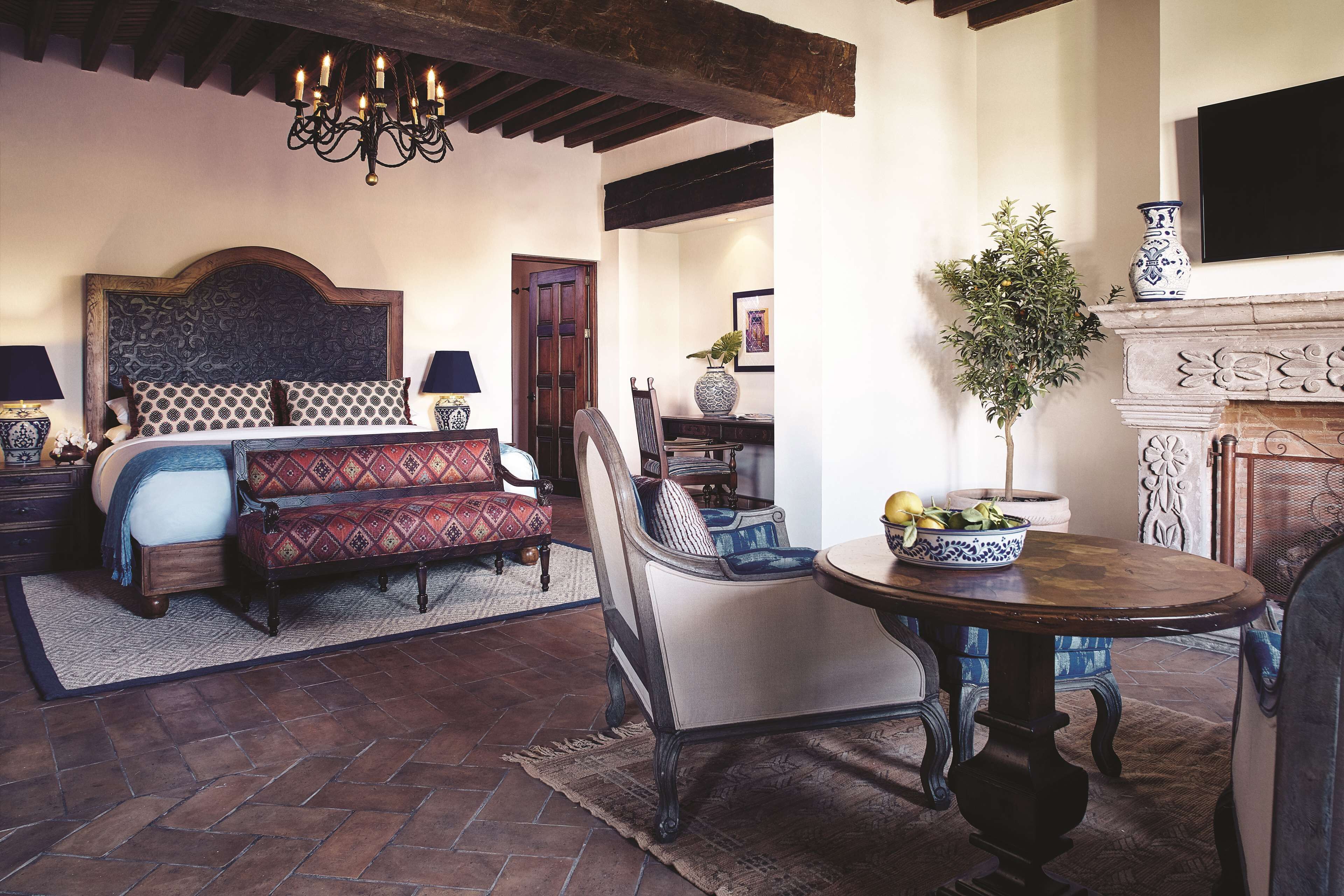 A bedroom with a large bed, a sofa, a dining table, and a fireplace.