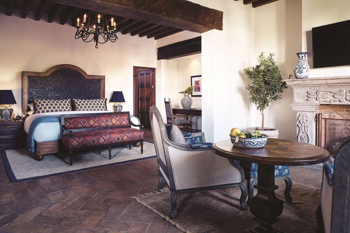 A bedroom with a large bed, a sofa, a dining table, and a fireplace.