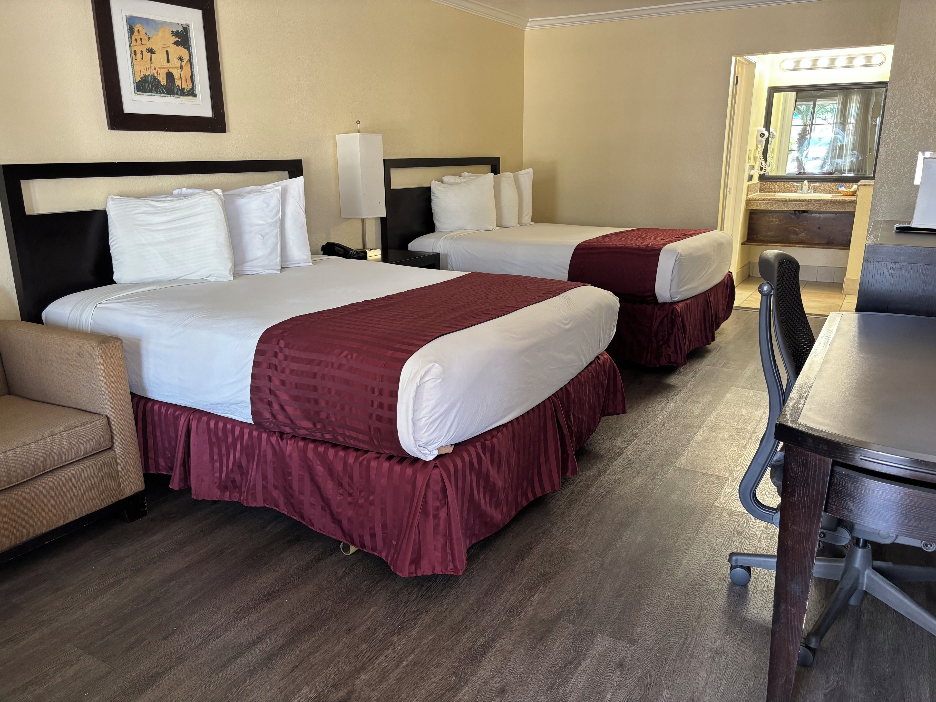 A hotel room with two beds, a desk, and a chair.