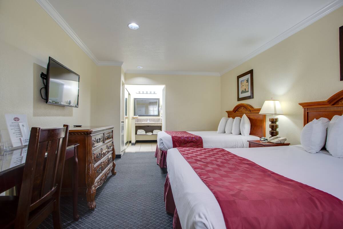 A hotel room with two beds, a desk, a chair, a dresser, a mirror, a lamp, and a telephone.