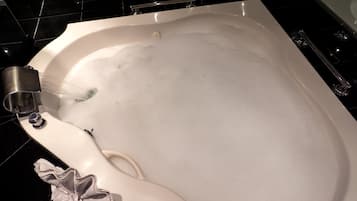 Una bañera con burbujas, un cabezal de ducha manual y una toalla.