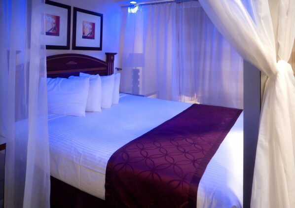 A neatly made bed with white linens and a purple blanket, a wooden headboard, and a bedside table with a lamp.