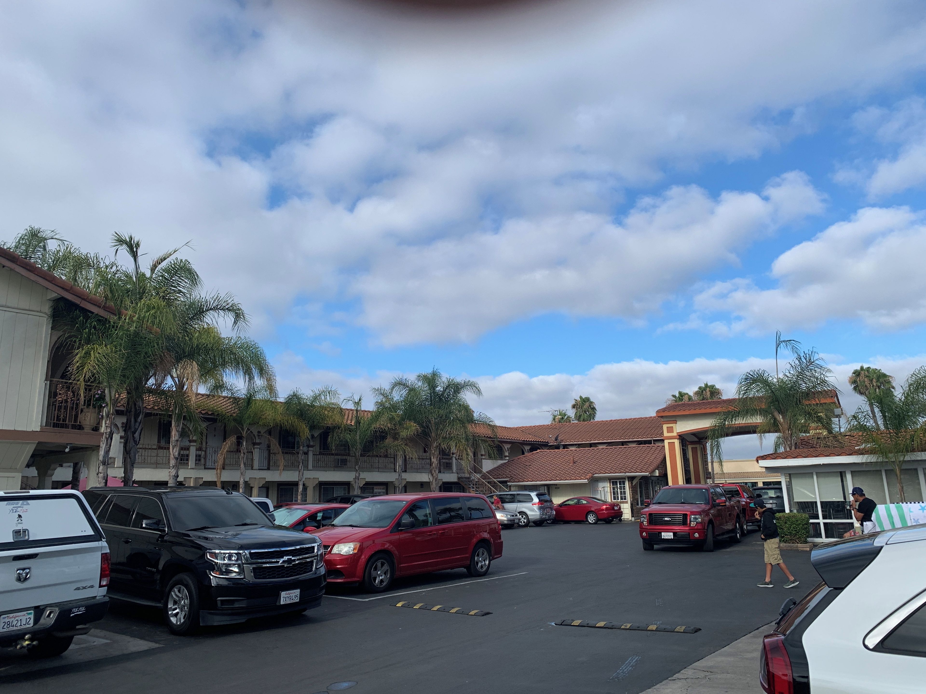 Un estacionamiento con varios autos, un edificio con techo de tejas rojas y palmeras.